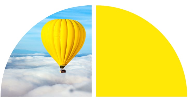 A yellow hot air balloon floats above the clowds against a blue sky.